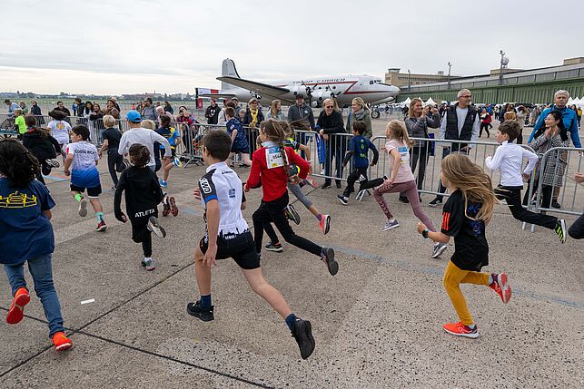 Bambini running towards the finish line, an airplane in the background