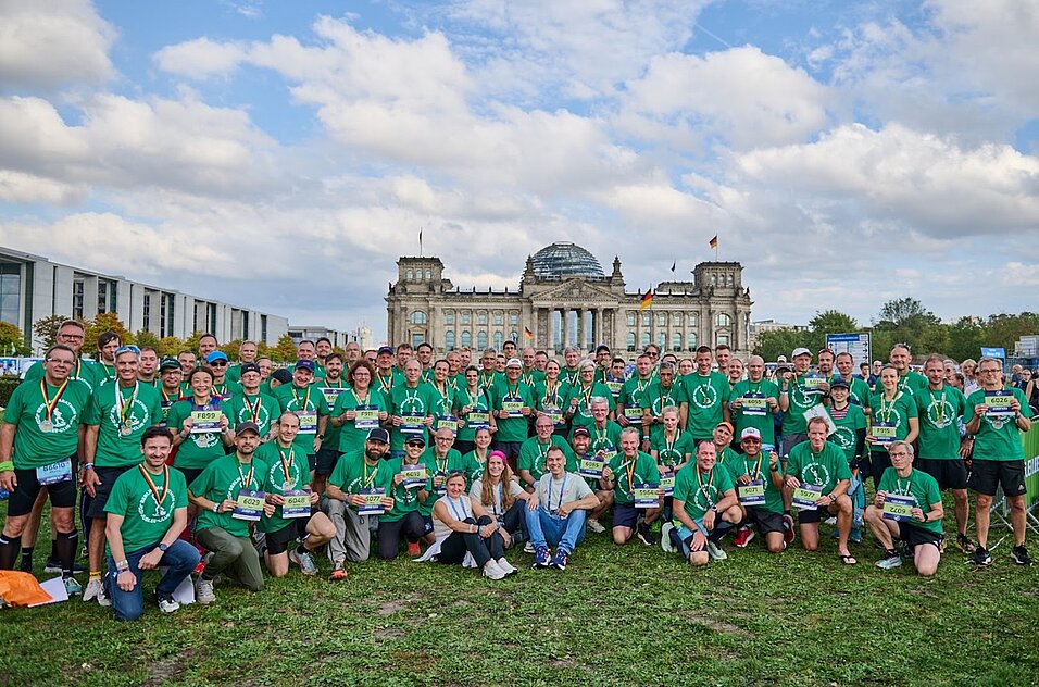 Läufer:innen in grünen Jubilee-T-Shirts auf der Reichstagswiese mit dem Reichstag gut sichtbar im Hintergrund.