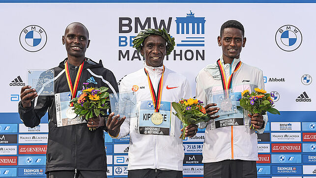 Die Männer bei der Siegerehrung. In der Mitte steht Eliud Kipchoge mit einem Lorbeerkranz auf dem Kopf, links neben ihm steht Mark Korir, rechts steht Tadu Abate.