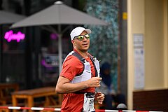 Mann mit Sonnenbrille und Baseball-Cap läuft bei der Veranstaltung "Die Generalprobe"; Er trägt eine Weste mit Wasserflaschen.