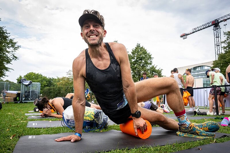 A man rolls sideways on a fascia roll; in the background, other people are doing exercises.