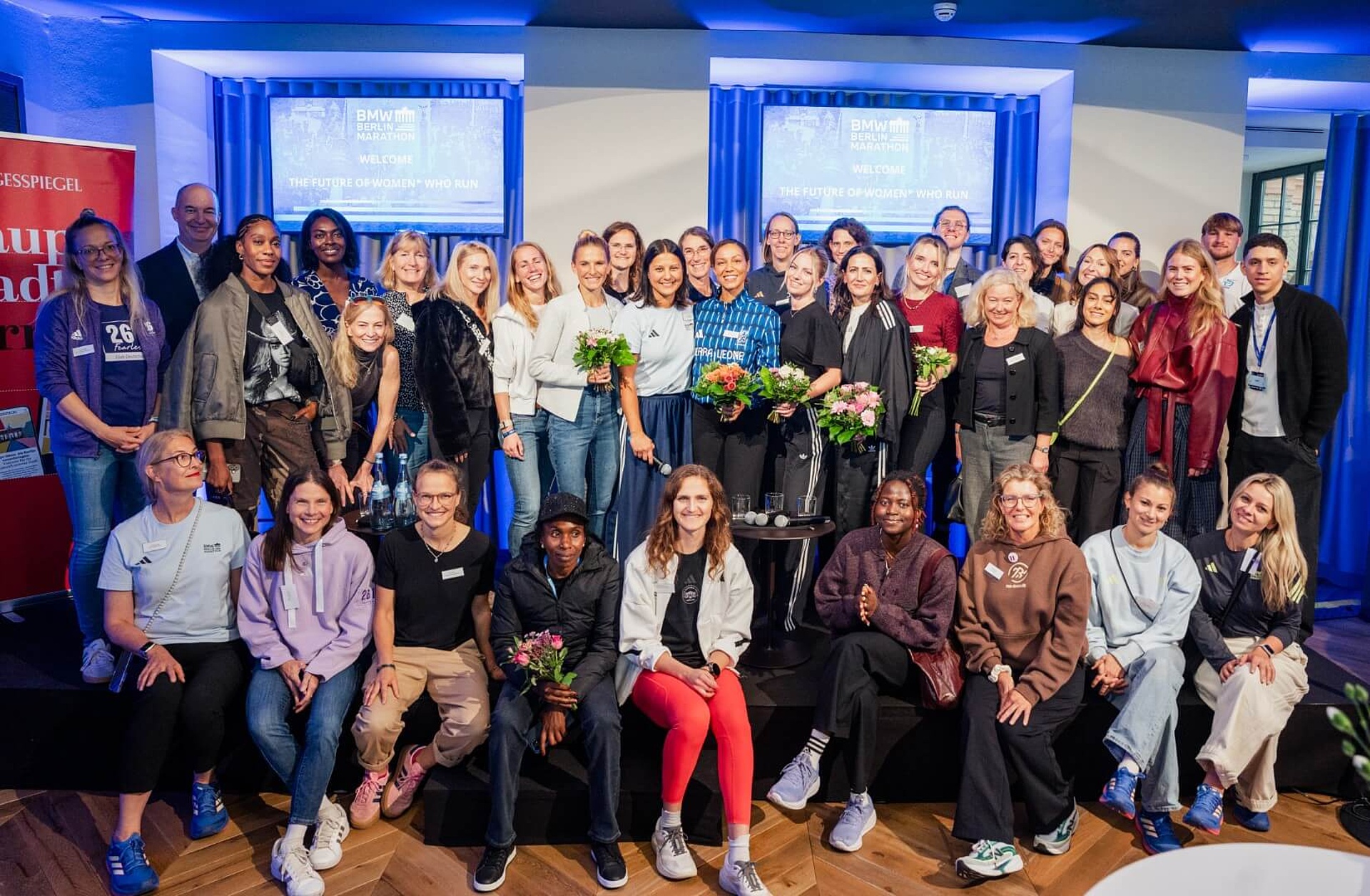 Group photo of about 30 people, almost all of whom are women. Some are holding bouquets of flowers.