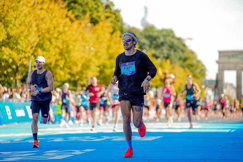 Harry Styles wearing sunglasses on the track; the Brandenburg Gate in the background.