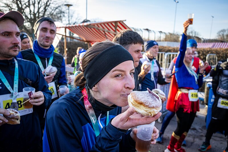 A woman happily bites into a jelly donut; other participants in the run can be seen in the background.