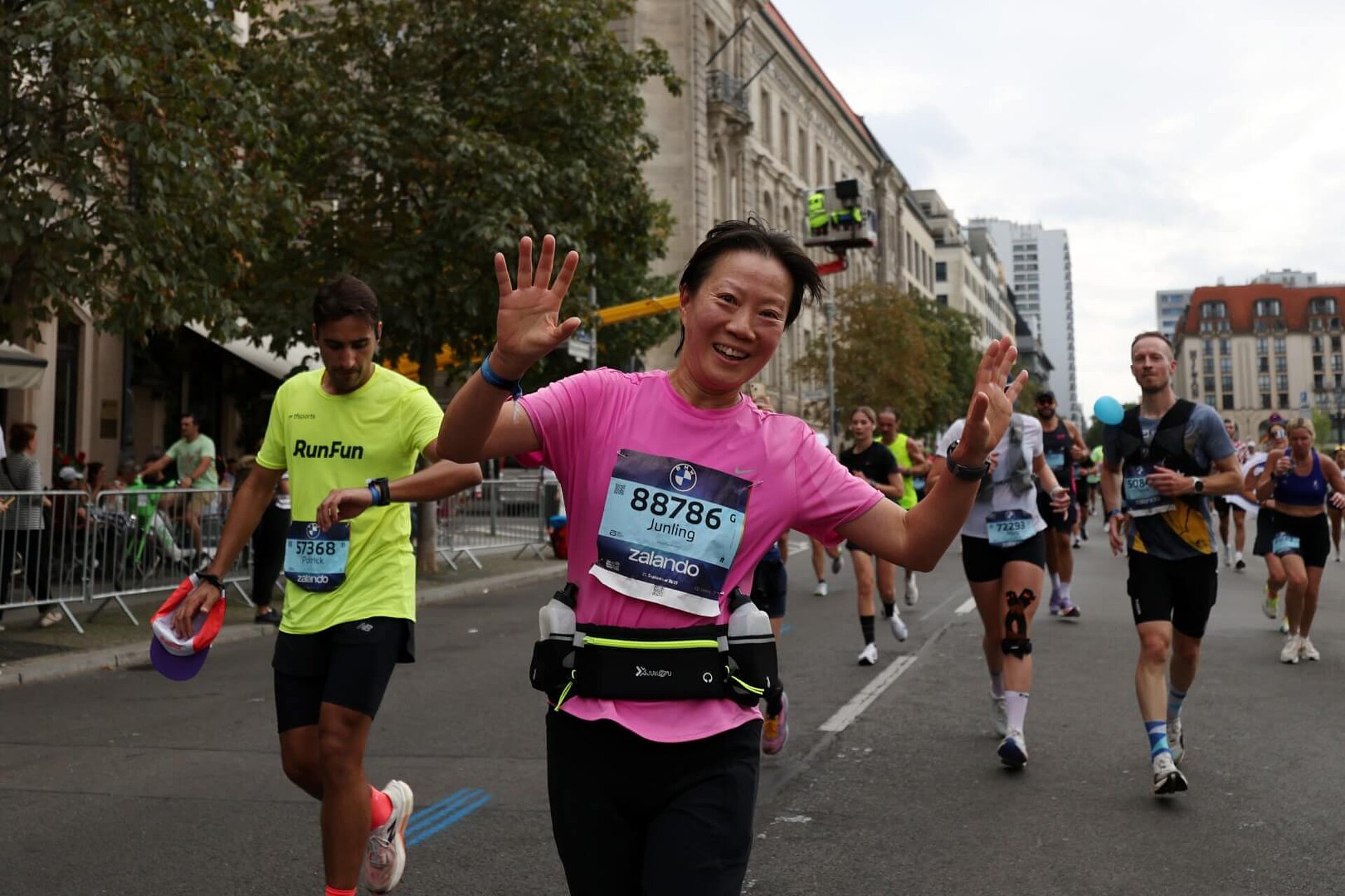 A runner wearing a hip belt with two small soft flasks in it. She is smiling and waving with her arms raised.