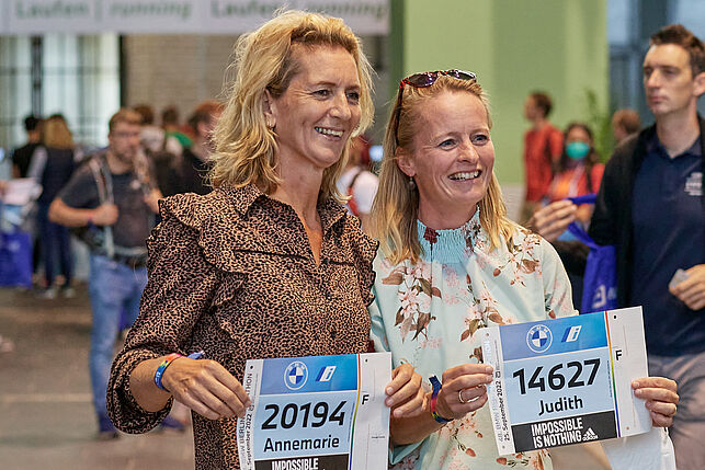 Two middle-aged runners hold their race numbers up to the camera at the Marathon Expo and take a happy souvenir photo.