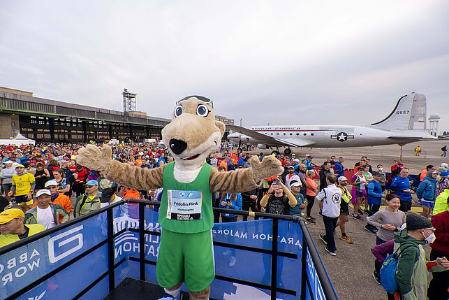 Frido welcomes with open arms the runners in front of an airplane.