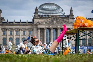 Finisherin des Marathons liegt vor dem Reichstag, trinkt etwas und hat ihre Beine hochgelegt.