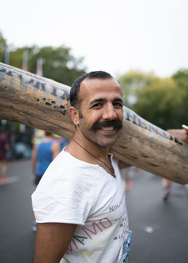Ein Teilnehmer traegt einen Holzstamm auf den Schultern, mit dem er an den Start des BMW BERLIN-MARATHON geht.