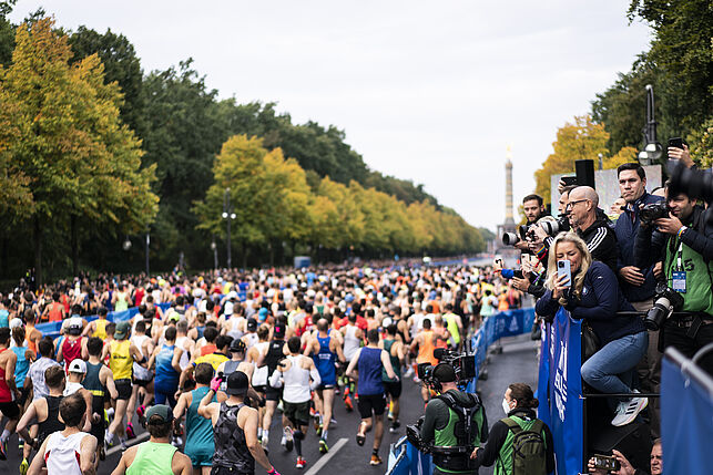 Eine große Anzahl von Laeufern und Laeuferinnen geht auf die Strecke des Marathons und wird von vielen Fotografen abgelichtet. Sie laufen auf die Siegessäule zu.