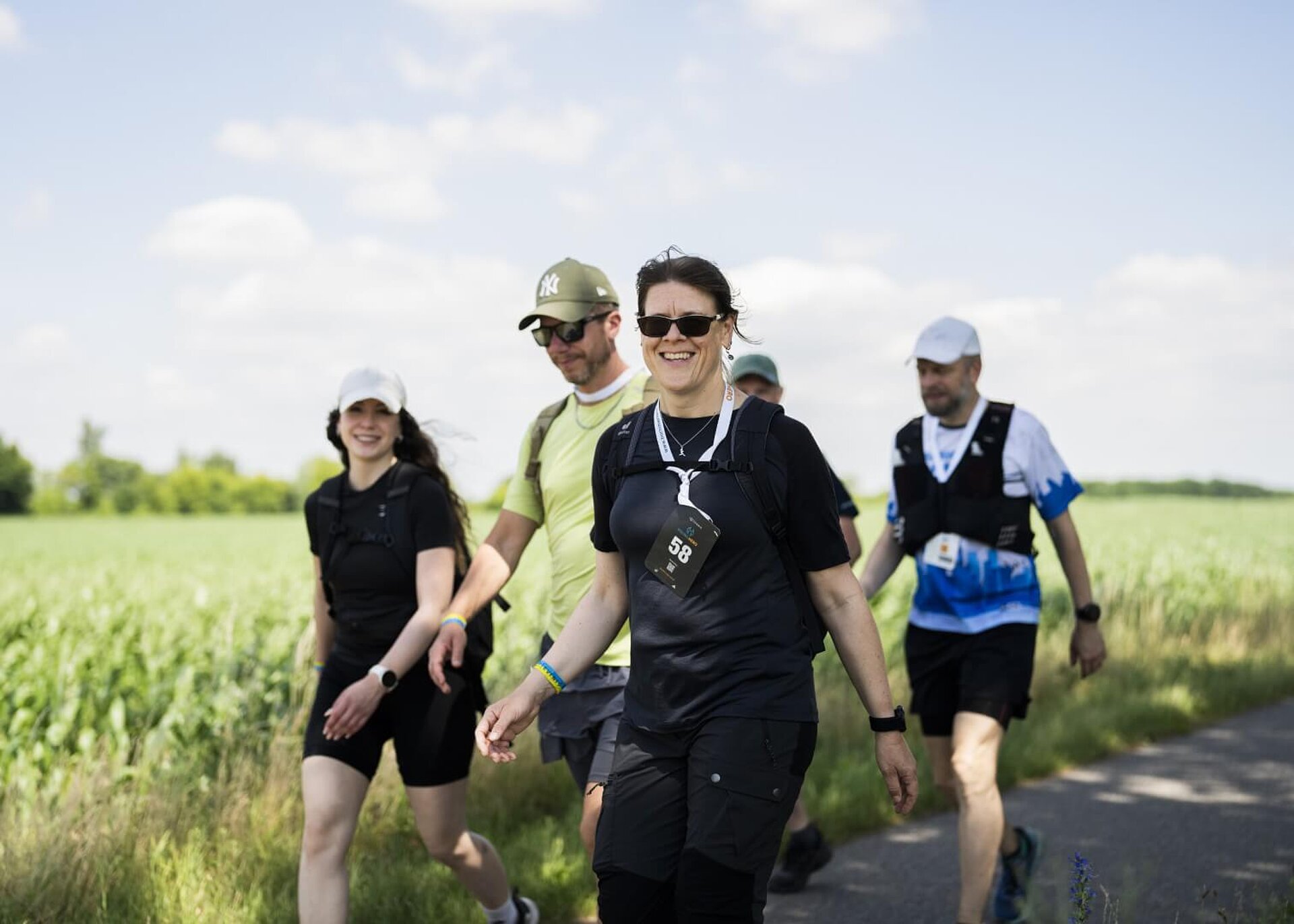 Kleine Gruppe an gut gelaunten Teilnehmer:innen wandern neben grünem Feld.