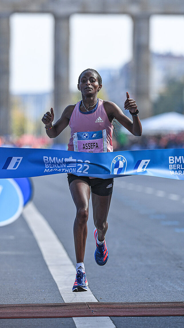 Tigist Assefa is the first woman to cross the finish line and gives the thumbs up.